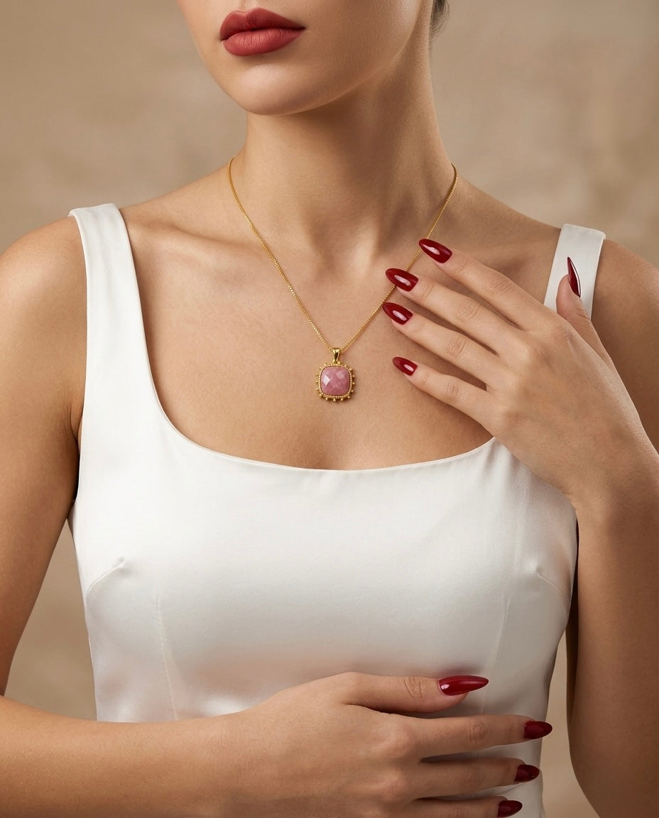 Woman wearing a gold necklace with a pink gemstone against a beige background
