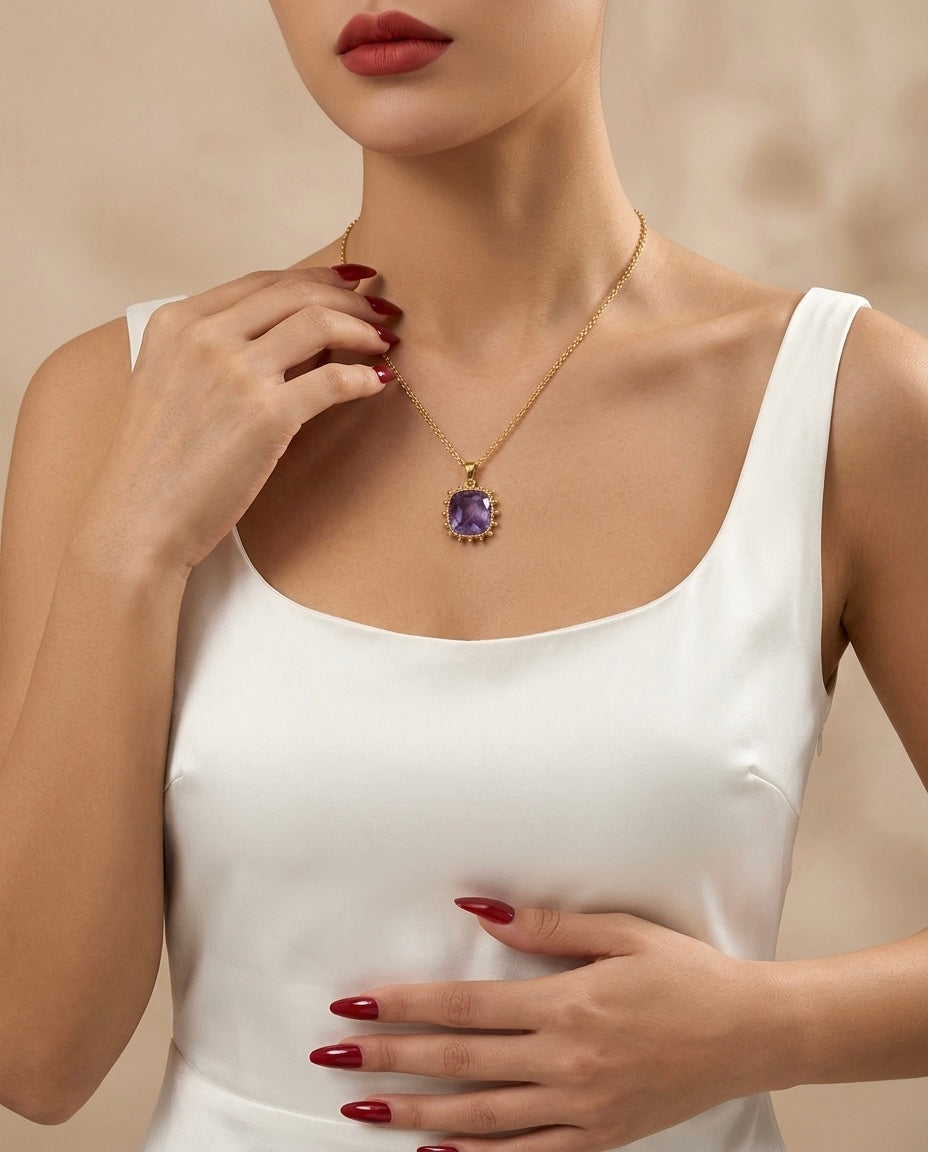 Woman wearing a gold necklace with a purple gemstone against a neutral background