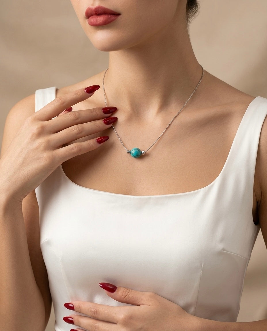 Woman wearing a necklace with a turquoise pendant against a neutral background