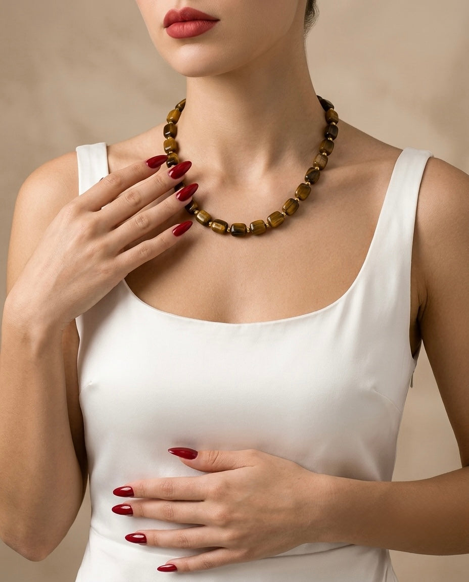 Woman wearing a white tank top and a brown beaded necklace against a beige background