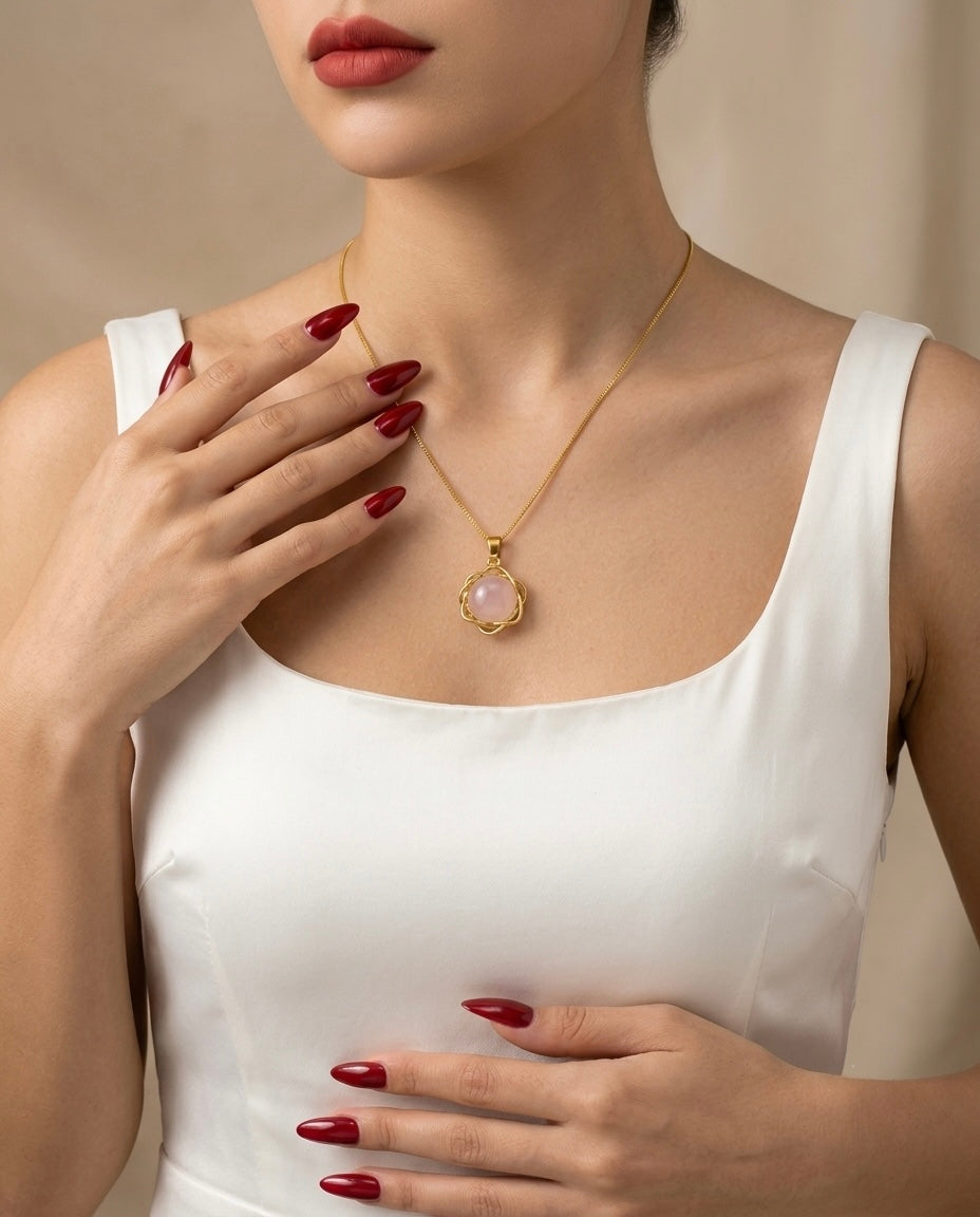 Woman wearing a gold necklace with a pink gemstone, hand touching the necklace.