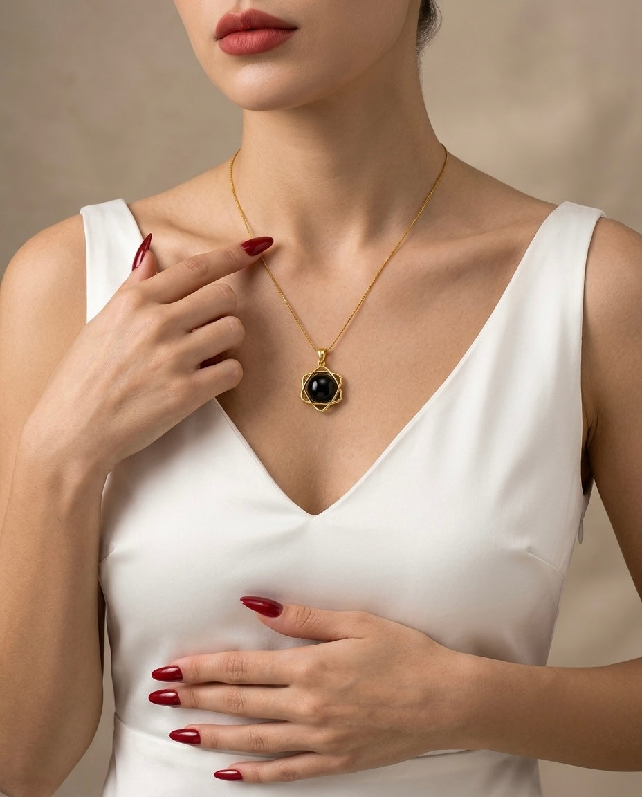 Woman wearing a gold necklace with a black pendant, holding it with her hand.