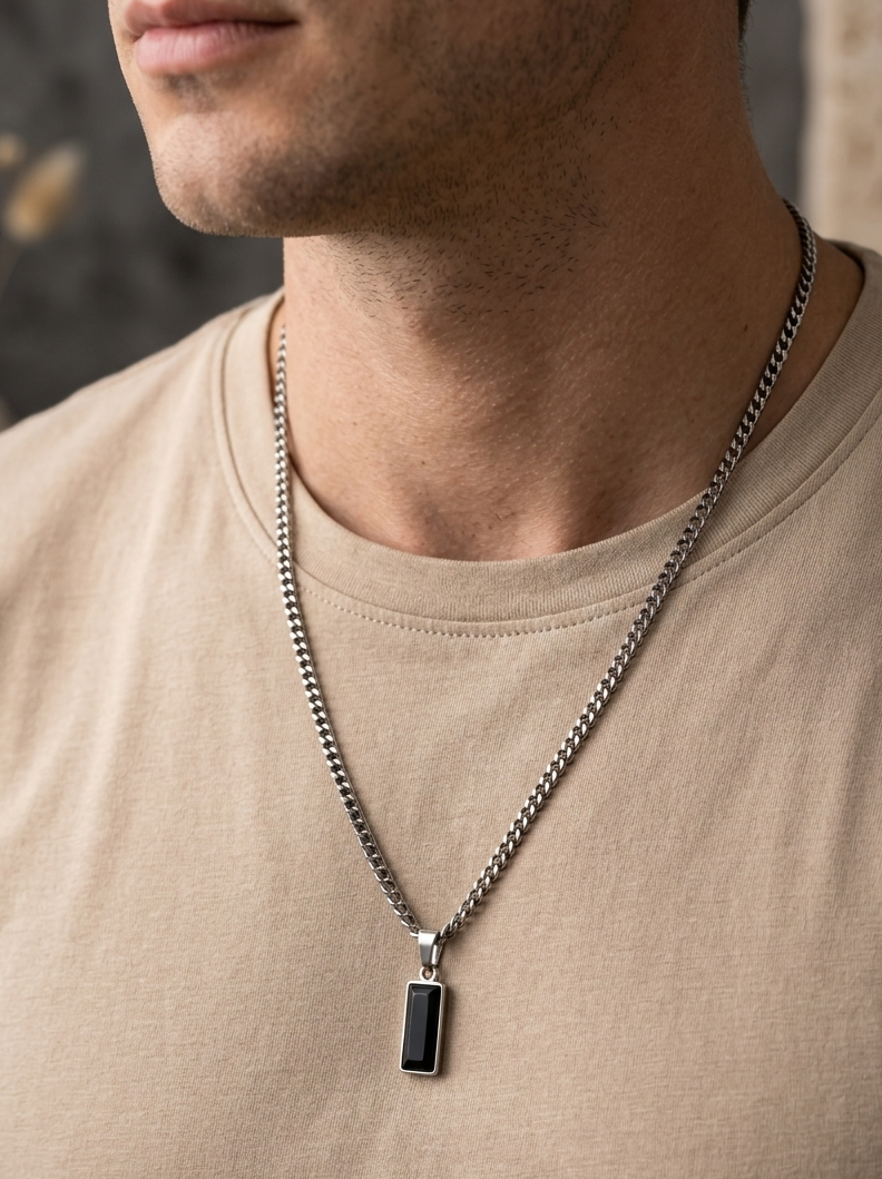 Man wearing a silver necklace with a black pendant on a neutral background