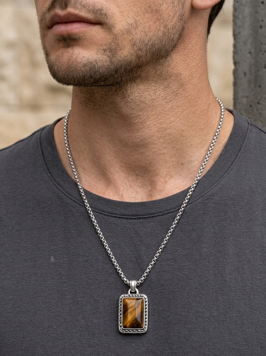 Man wearing a necklace with a rectangular pendant featuring a brown gemstone.
