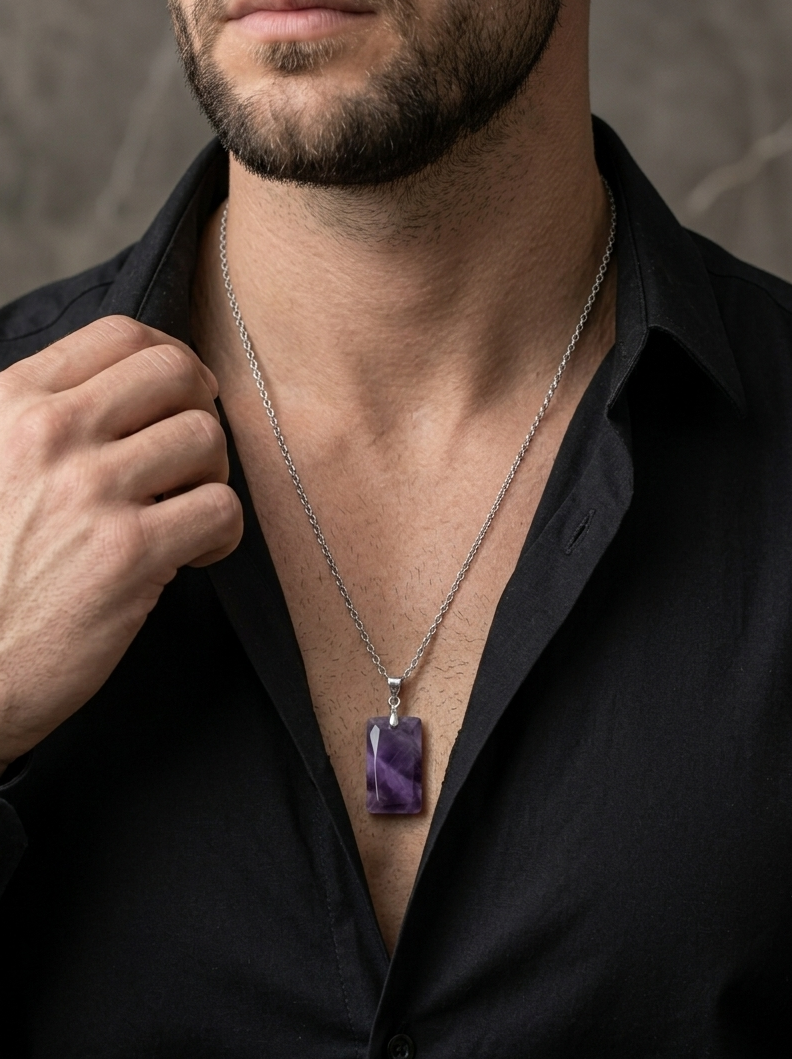Man wearing a black shirt with a silver necklace featuring a purple pendant against a neutral background