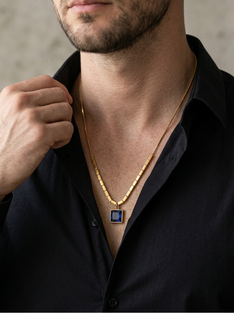 Man wearing a gold necklace with a blue pendant against a neutral background
