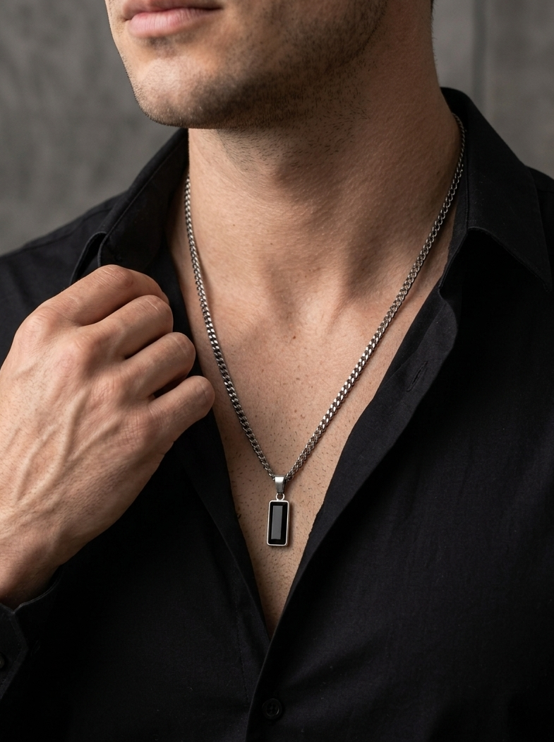 Man wearing a black shirt with a silver necklace featuring a rectangular pendant.