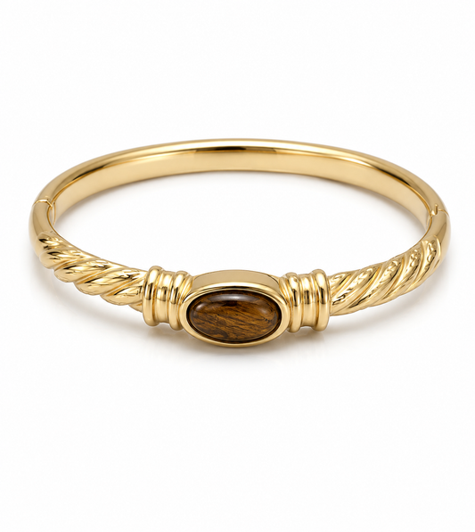 A gold bangle bracelet featuring a central oval inlay of brown tiger's eye stone, set against a plain white background.