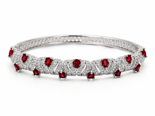 A silver-toned tennis-style bangle bracelet featuring a row of round-cut red gemstones and small clear stones in an openwork pattern, set against a plain white background.