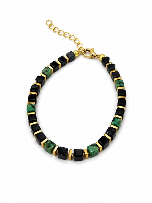 A beaded necklace featuring alternating black and green marbled rectangular beads, separated by gold spacer rings, with a gold clasp and extender chain on a white background.