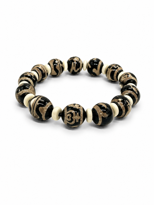 A beaded stretch bracelet featuring glossy black and cream beads with carved symbols and swirl patterns, displayed on a clean white background.
