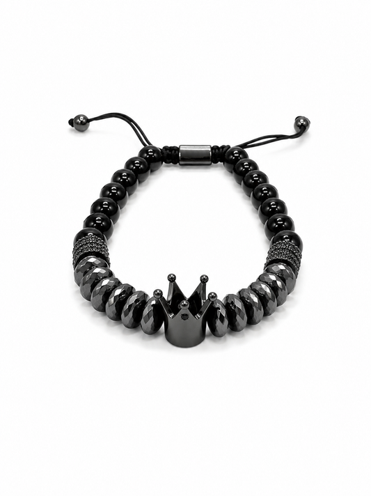 A black beaded bracelet featuring a central crown-shaped charm, textured spacer beads, and an adjustable sliding cord closure, shown on a plain white background.