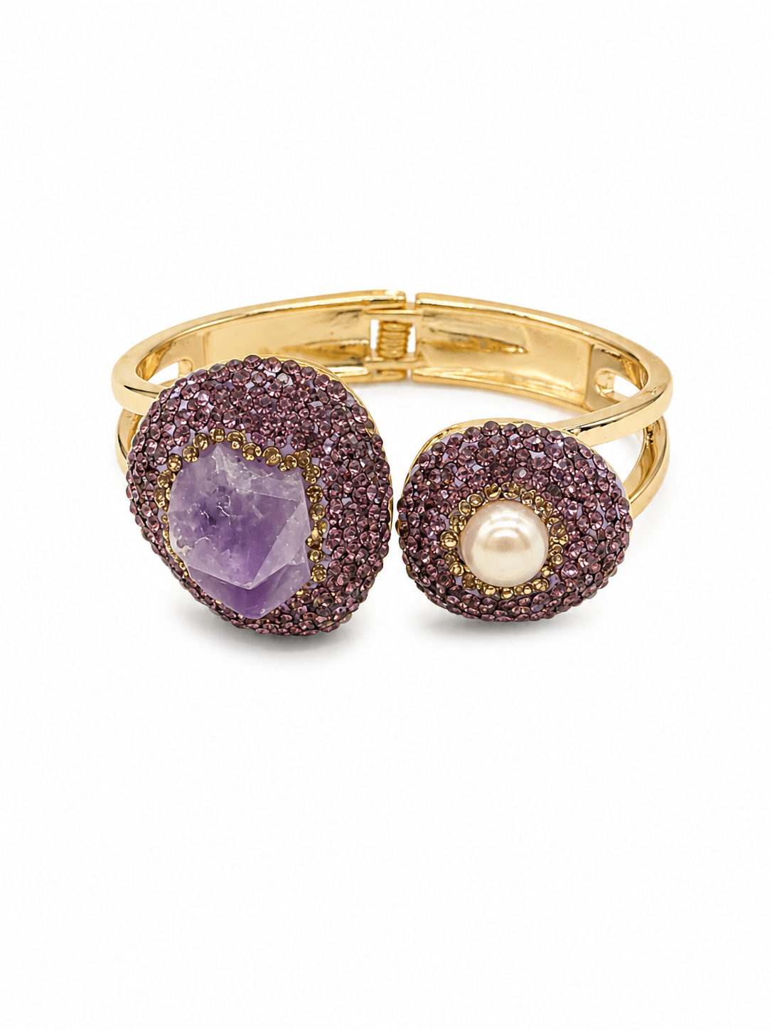 A gold-tone open cuff ring featuring two round pavé-set bezels: one with a faceted purple amethyst stone and the other with a white pearl, both surrounded by textured dark pinkish-purple crystals, shown on a white background.
