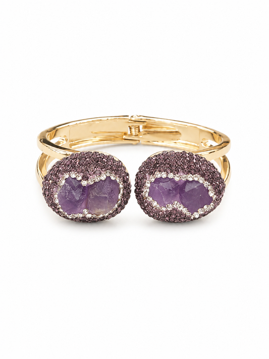 A gold-tone cuff bracelet featuring two oval bezel-set amethyst crystal clusters surrounded by pavé diamonds, shown on a plain white background.