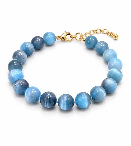 A beaded bracelet made of round light blue and medium blue polished beads with a gold clasp and extension chain, shown on a clean white background.