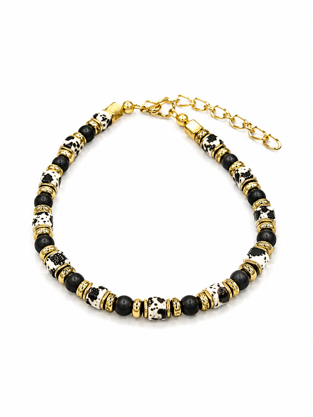 A beaded necklace with alternating black beads, white beads with black spots, and textured gold spacer beads, finished with a gold clasp and extender chain.