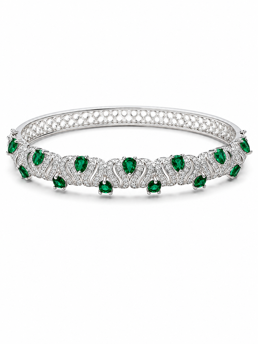 A silver tennis-style bangle bracelet featuring a row of green emerald-cut gemstones and pavé-set clear stones, shown on a plain white background.