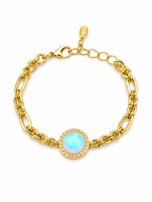 A gold chain bracelet with a central oval light blue opal-like stone surrounded by a halo of small clear crystals, shown on a plain white background.