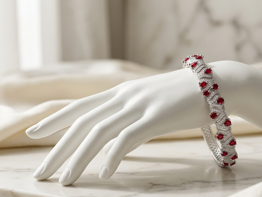 A silver-toned bangle bracelet with red gemstones, displayed on a white mannequin hand over a light marble surface.