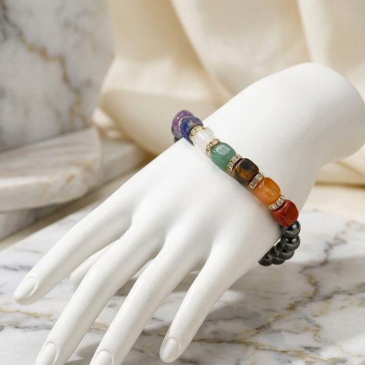 A multicolor beaded bracelet with gemstone-like round beads and metallic spacer rings, displayed on a white mannequin hand over a marble surface.