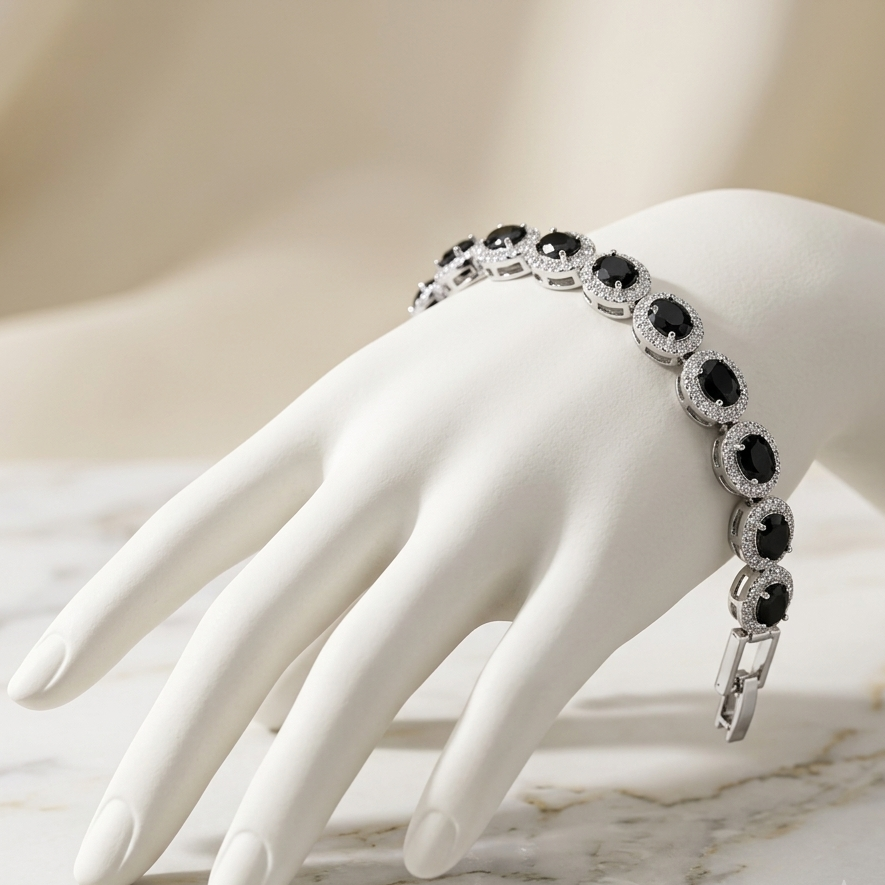 A silver-toned bracelet with oval black stones and clear accent stones, displayed on a white mannequin hand over a light marble surface.