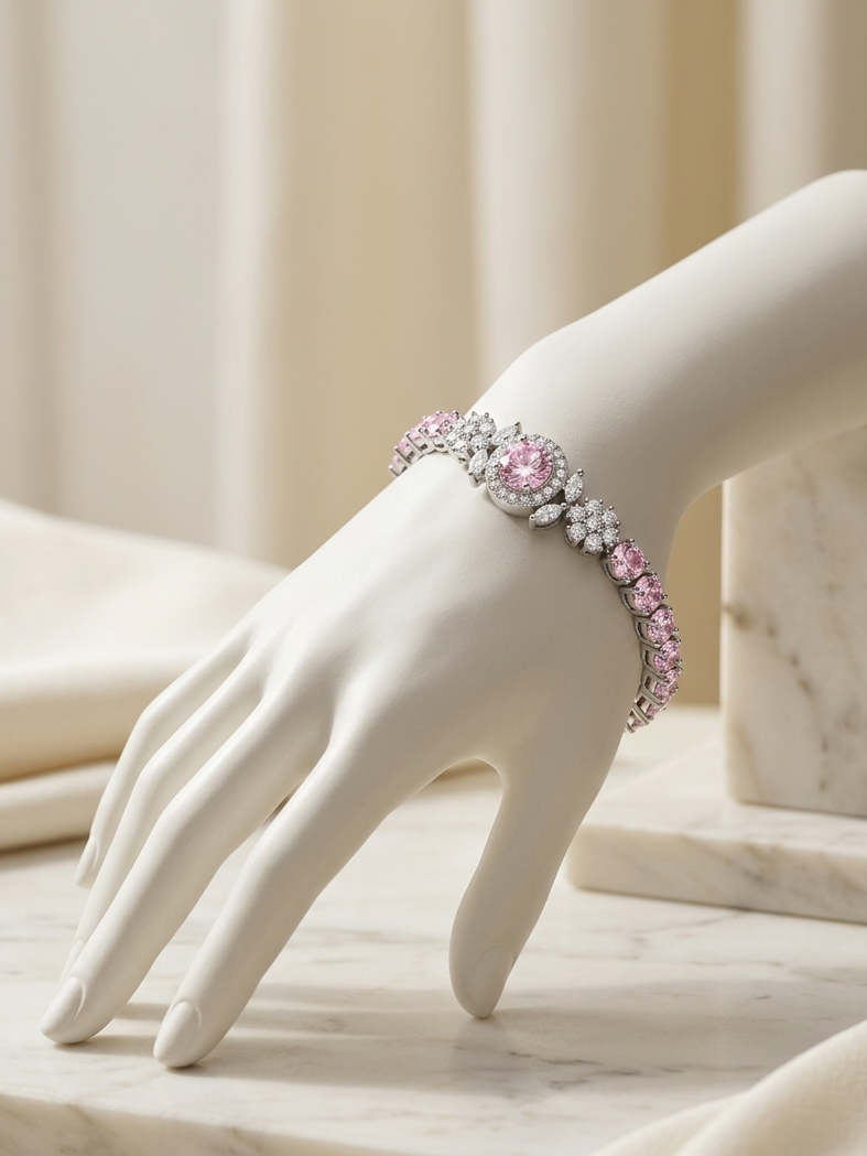A close-up of a white mannequin hand wearing a silver-toned bracelet adorned with pink gemstones and clear stones, set against a soft beige draped fabric background.