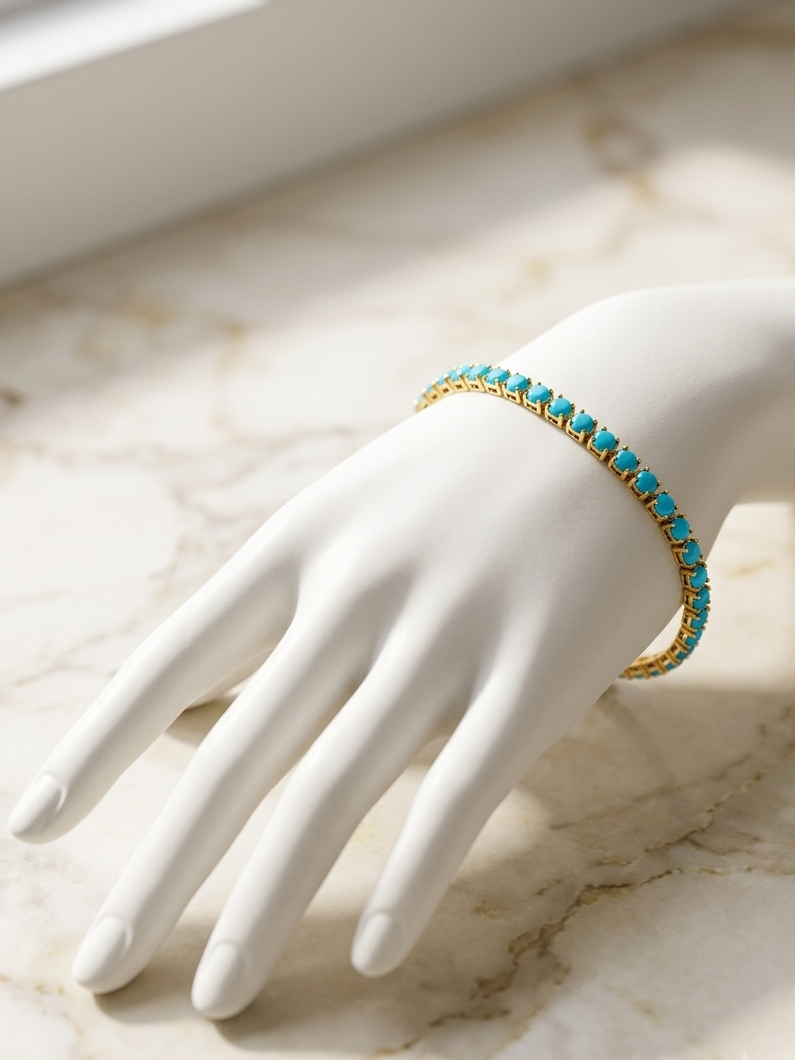 A gold bracelet with small turquoise blue stones, displayed on a white mannequin hand over a light marble surface.