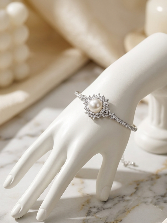 A silver-toned ring with a central white pearl and surrounding clear stones, displayed on a white mannequin hand over a marble surface.