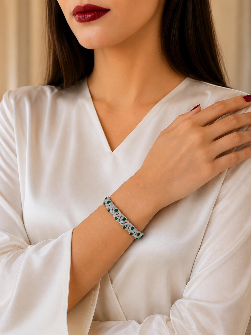 A close-up of a woman wearing a white satin V-neck top and a patterned bracelet with green, white, and black details on her wrist, set against a soft beige background.