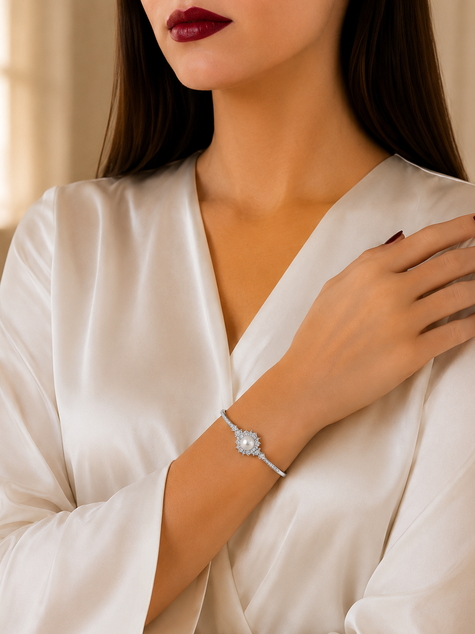 A woman wearing a white satin robe and dark red lipstick, showcasing a delicate silver-toned bangle bracelet with a central clear crystal on her wrist.