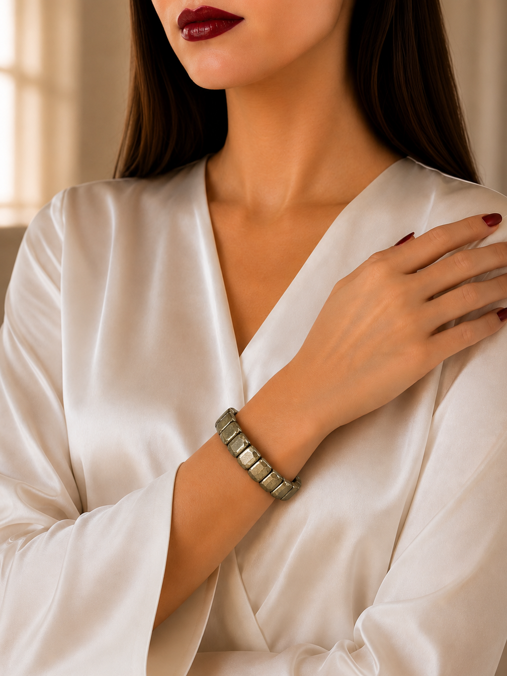 A close-up of a woman wearing a textured metallic silver link bracelet on her wrist, styled with a white satin robe.