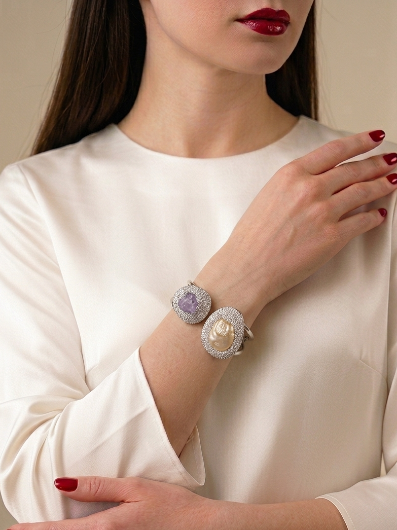 A close-up of a woman wearing a cream satin blouse and red nail polish, showcasing a double-row bracelet with oval cabochon gemstones on her wrist.
