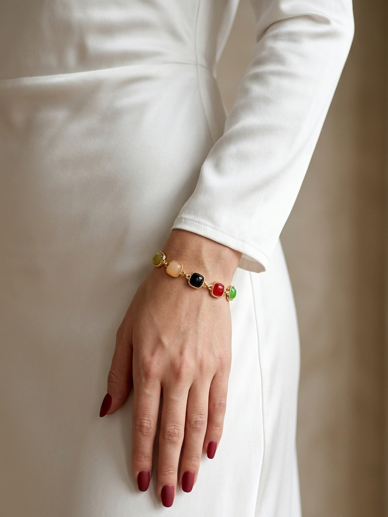 A close-up of a person wearing a delicate beaded bracelet on their wrist, dressed in a white long-sleeve dress. The bracelet features small, colorful round beads in yellow, black, red, and green.