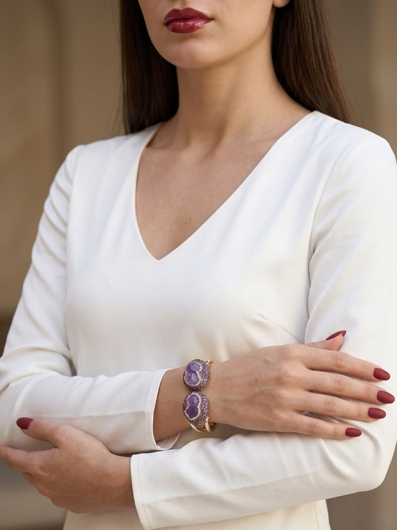 A woman wearing a white long-sleeve V-neck dress, showcasing a gold-toned double-band bracelet with purple oval stones on her wrist.