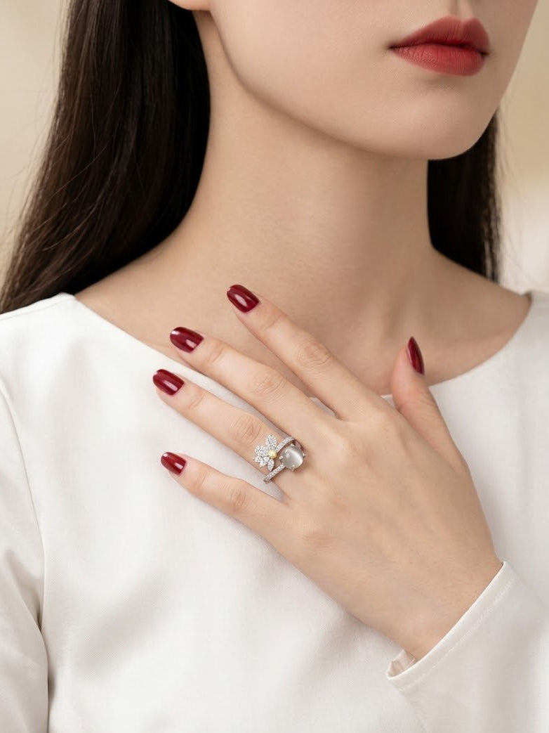 A close-up of a woman wearing a silver ring with a heart-shaped clear gemstone, styled with dark red nail polish and a white top.