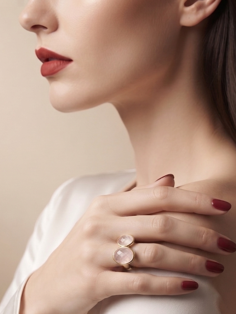 A close-up lifestyle shot of a woman wearing a gold ring with two round pale pink gemstones, resting her hand on her shoulder.