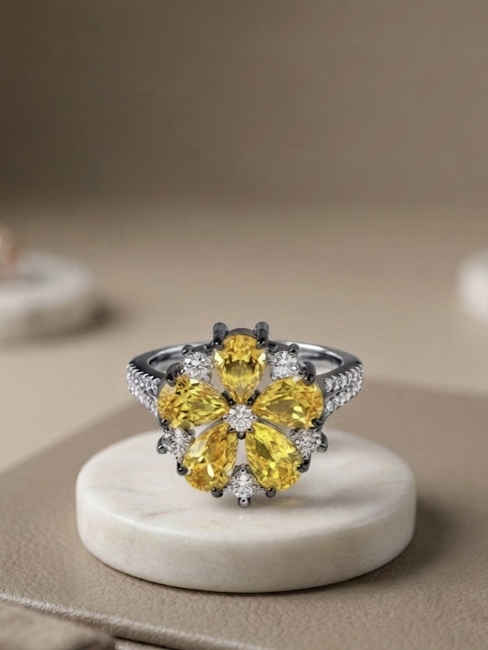 A floral cluster ring featuring large yellow gemstones and small clear stones on a silver-toned band, displayed on a round white marble stand against a warm beige background.