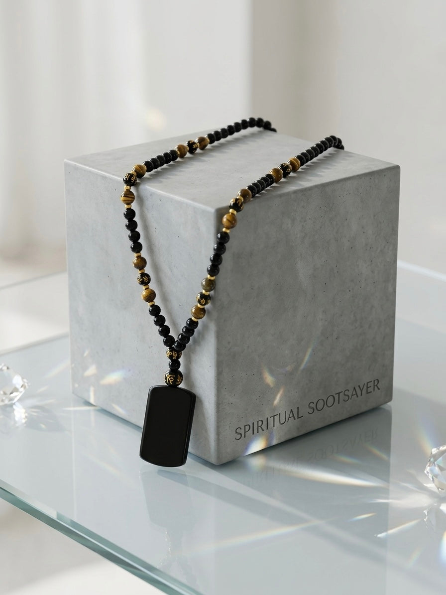 A beaded necklace with a black rectangular pendant draped over a gray display box. The necklace features black and metallic gold beads, with the brand name 'SPIRITUAL SCOTSAVER' printed on the box.