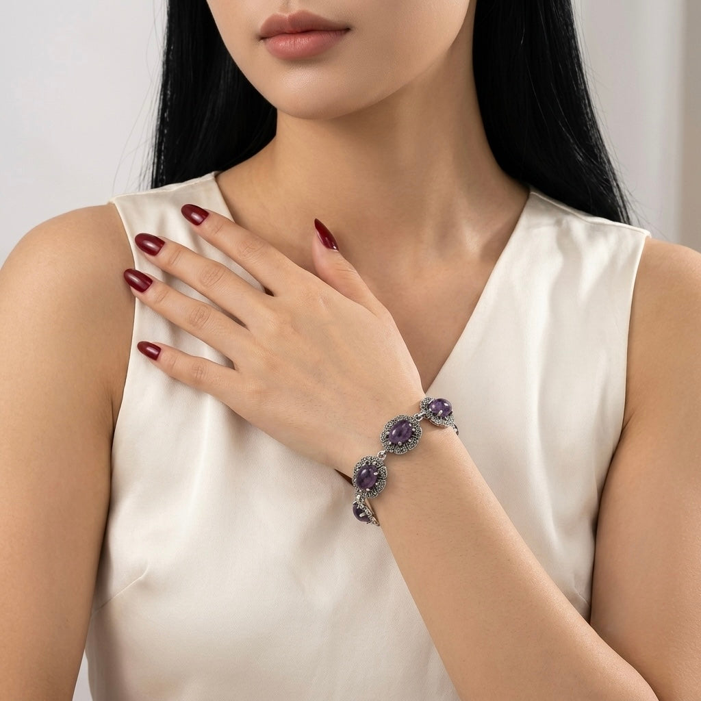 A close-up of a woman wearing a silver-toned bracelet with purple gemstone clusters, styled with a white satin top.