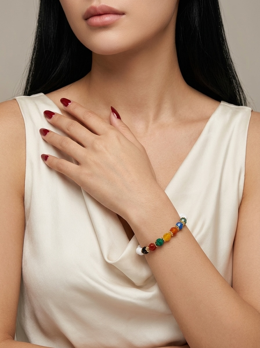 A close-up of a woman wearing a colorful beaded bracelet on her wrist, paired with a cream-colored satin top. The bracelet features multiple small, round beads in red, orange, yellow, green, blue, and white.