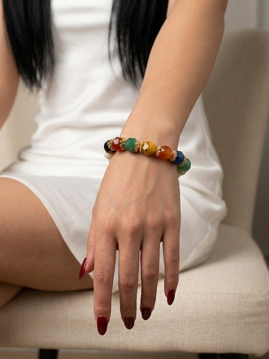 A close-up of a person's hand and wrist wearing a beaded stretch bracelet with colorful round beads, seated on a light beige chair.