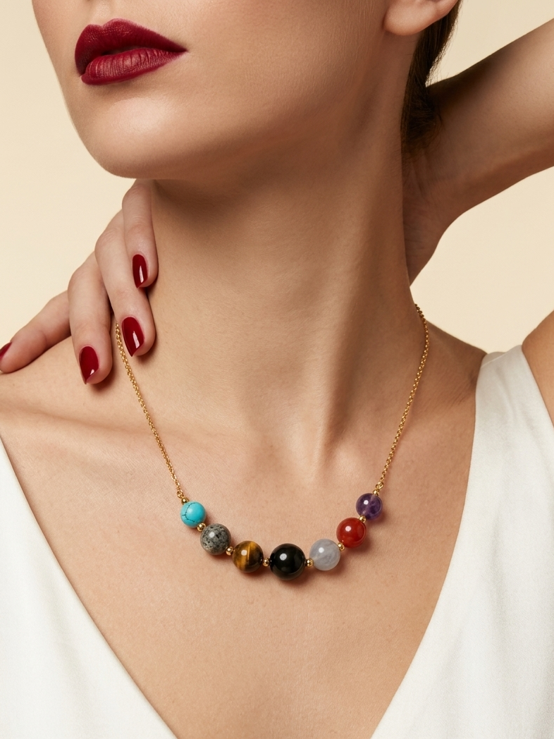 A close-up of a model wearing a gold necklace with a row of colorful round gemstone beads, paired with a white top and red lipstick.