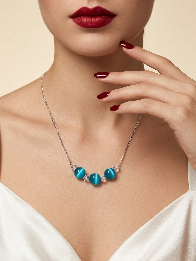 A close-up of a model wearing a silver necklace with four glossy turquoise-blue beads at the center, styled with a white satin top and dark red lipstick.