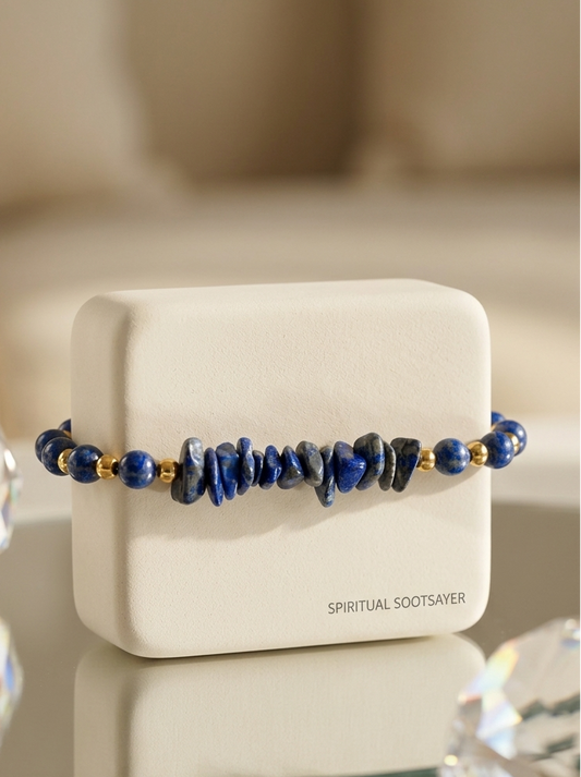 A beaded bracelet with dark blue lapis lazuli stones and small gold spacer beads, displayed on a white jewelry box labeled 'SPIRITUAL SOOTSAYER'.
