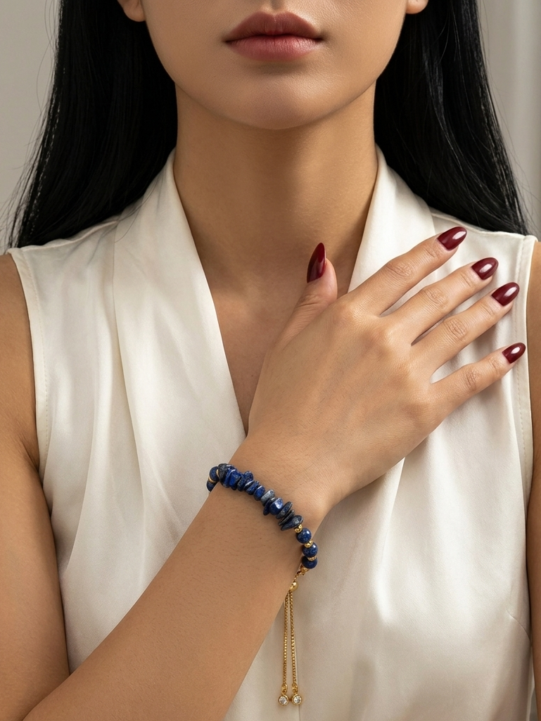 A close-up of a woman wearing a dark blue beaded bracelet with a gold tassel charm, paired with a white satin sleeveless top.