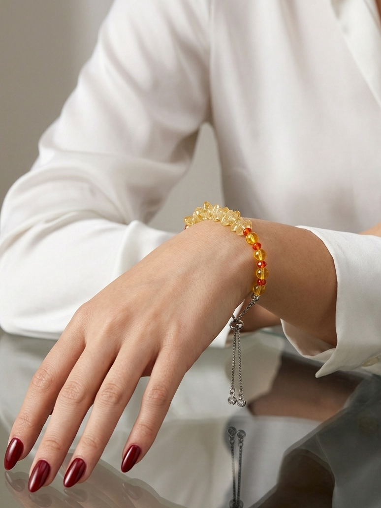 A close-up of a person's hand and wrist wearing a beaded bracelet with yellow and red beads, paired with a silver chain tassel, while wearing a white long-sleeve blouse.