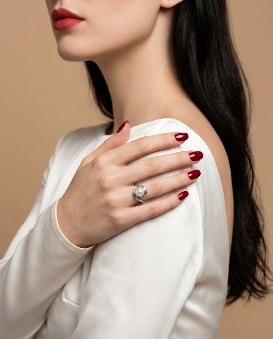 A close-up lifestyle shot of a model wearing a silver ring with a large white pearl on her finger, dressed in a white top against a warm beige background.