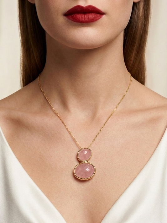 A close-up of a model wearing a delicate gold chain necklace with two stacked oval pink gemstones, styled with a white v-neck top.