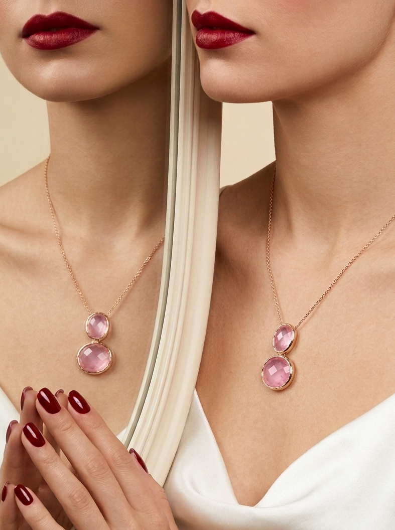 A close-up lifestyle shot of a model wearing a rose gold necklace with two pink gemstones, shown alongside a mirror reflection.