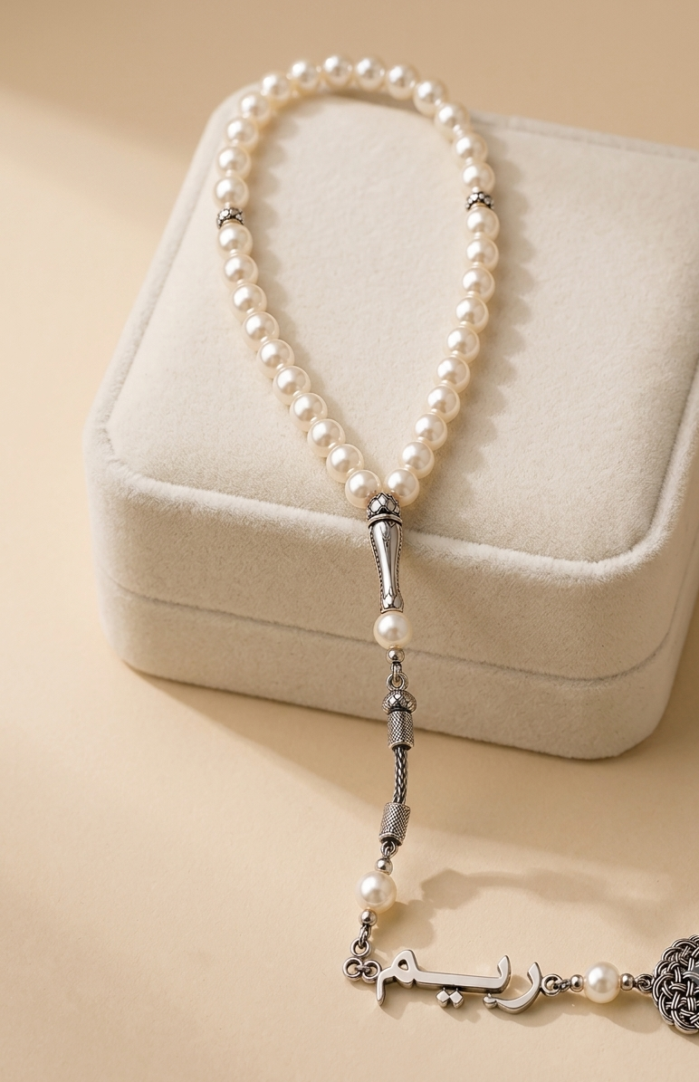 A pearl and silver beaded necklace with a detailed anchor charm and textured spherical accent, displayed on a cream-colored velvet jewelry box.